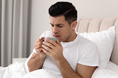 Photo of Sick man with cup of hot drink in bed at home