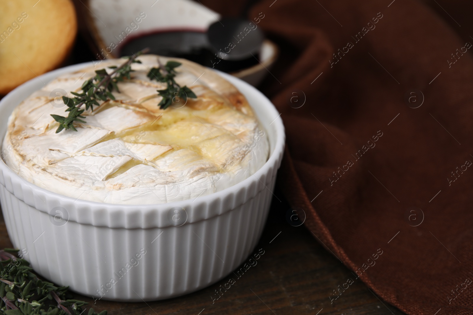 Photo of Tasty baked camembert and thyme in bowl on wooden table, closeup. Space for text