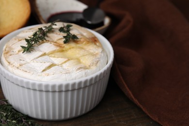 Tasty baked camembert and thyme in bowl on wooden table, closeup. Space for text