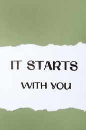 Photo of Sheet of paper with phrase It Starts With You on green background, top view