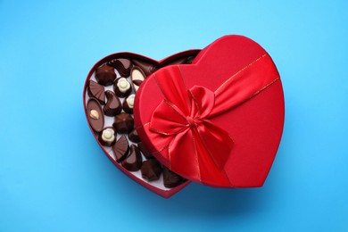 Heart shaped box with delicious chocolate candies on light blue background, top view