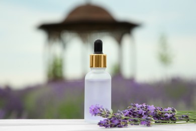 Bottle of essential oil and lavender flowers on white wooden table in field