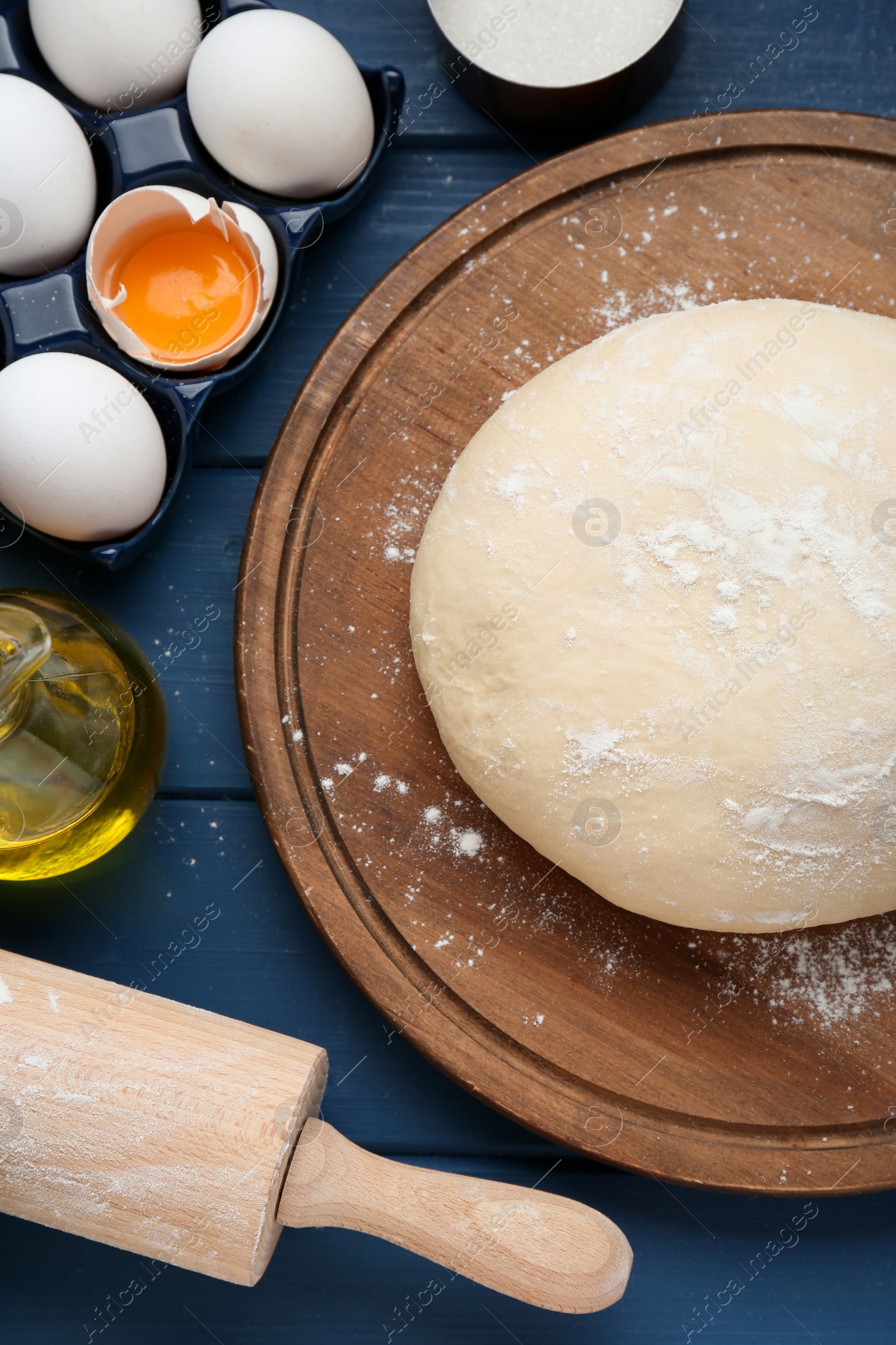 Photo of Fresh yeast dough and ingredients on blue wooden table, flat lay