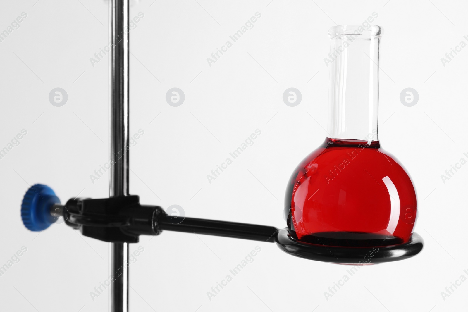 Photo of Retort stand and laboratory flask with liquid on white background, closeup