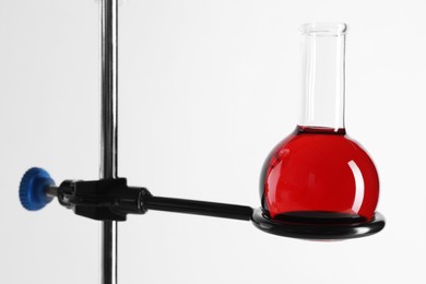 Photo of Retort stand and laboratory flask with liquid on white background, closeup
