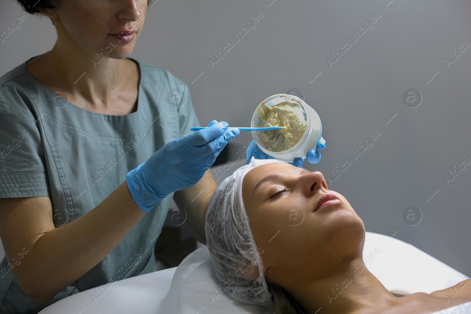 Photo of Cosmetologist applying mask on client's face in spa salon