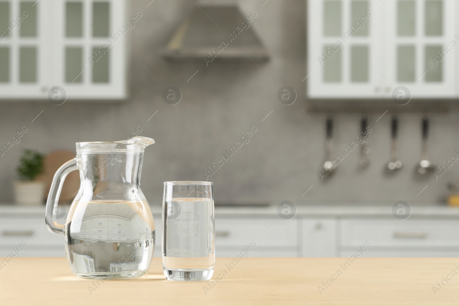 Photo of Glass and jug with water on wooden table in kitchen, space for text