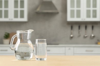 Glass and jug with water on wooden table in kitchen, space for text