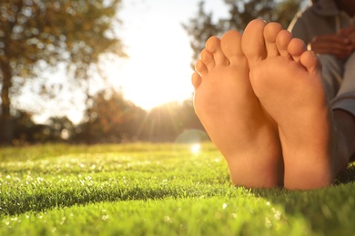 Man sitting barefoot on fresh green grass outdoors, closeup