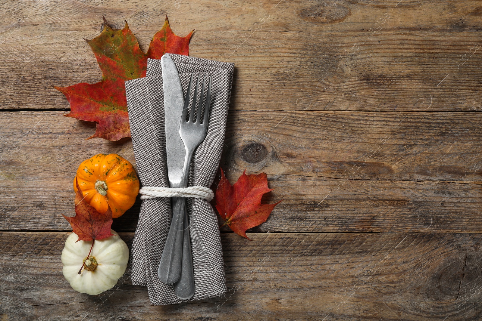 Photo of Thanksgiving table setting. Cutlery, napkin, autumn leaves and pumpkins on wooden background, flat lay with space for text