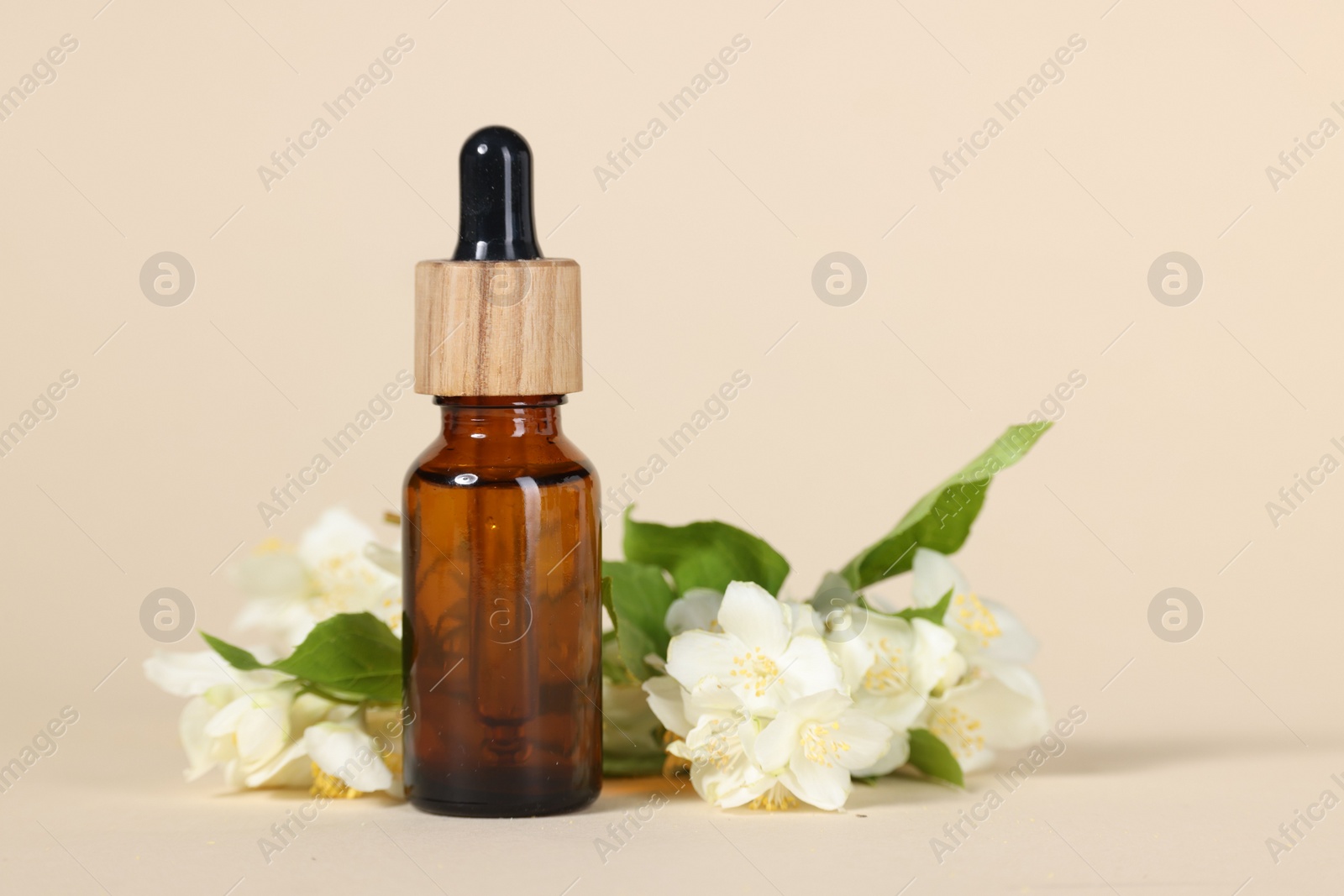 Photo of Essential oil in bottle and beautiful jasmine flowers on beige background, closeup