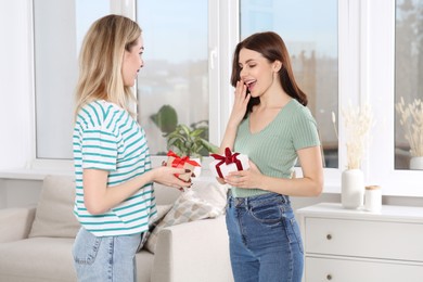 Smiling young women presenting gifts to each other at home