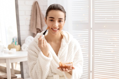 Young woman applying natural scrub on face in bathroom