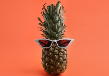 Photo of Funny face made of pineapple and sunglasses on coral background. Vacation time