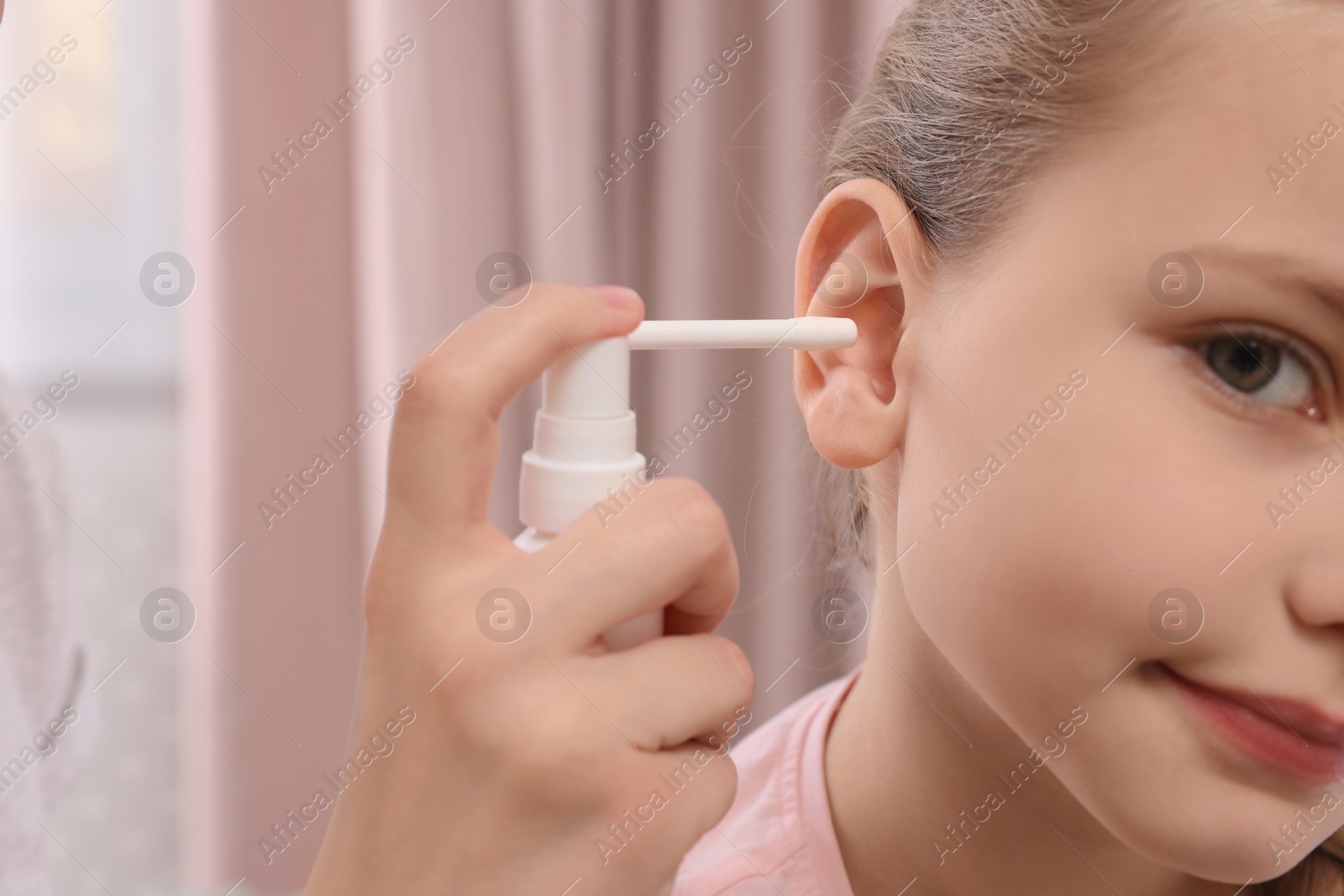Photo of Mother spraying medication into daughter's ear at home, closeup