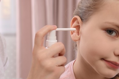 Mother spraying medication into daughter's ear at home, closeup