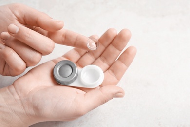 Woman holding contact lens and case on light background, closeup