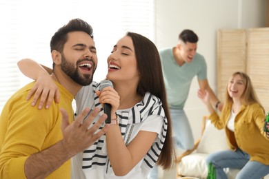 Photo of Happy couple singing karaoke with friends at home