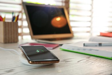 Photo of Mobile phone with wireless charger on white wooden table. Modern workplace accessory