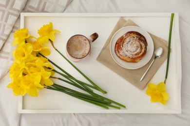 Bouquet of beautiful daffodils, bun and coffee on bed, top view