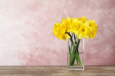 Bouquet of daffodils in vase on table against color background, space for text. Fresh spring flowers