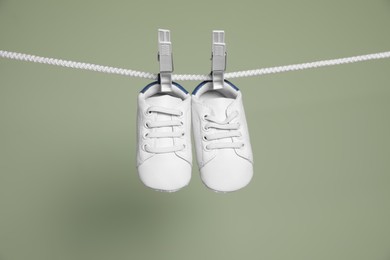 Cute small baby shoes hanging on washing line against green background