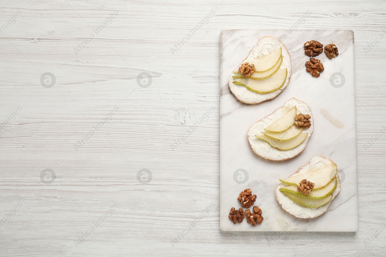 Photo of Delicious bruschettas with ricotta cheese, pears and walnuts on white wooden table, top view. Space for text