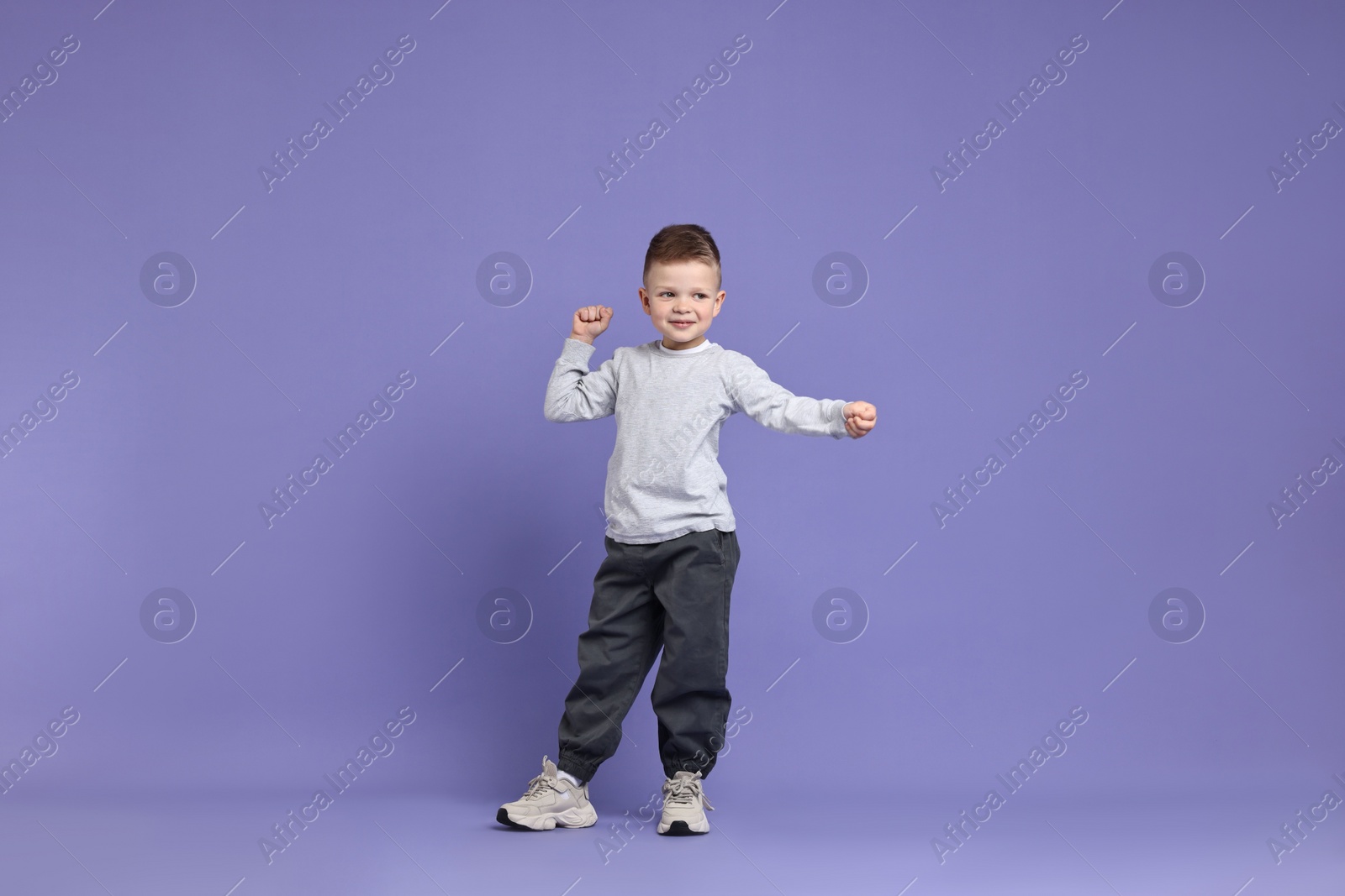 Photo of Happy little boy dancing on violet background