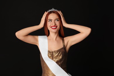 Photo of Beautiful young woman with tiara and ribbon in dress on black background. Beauty contest
