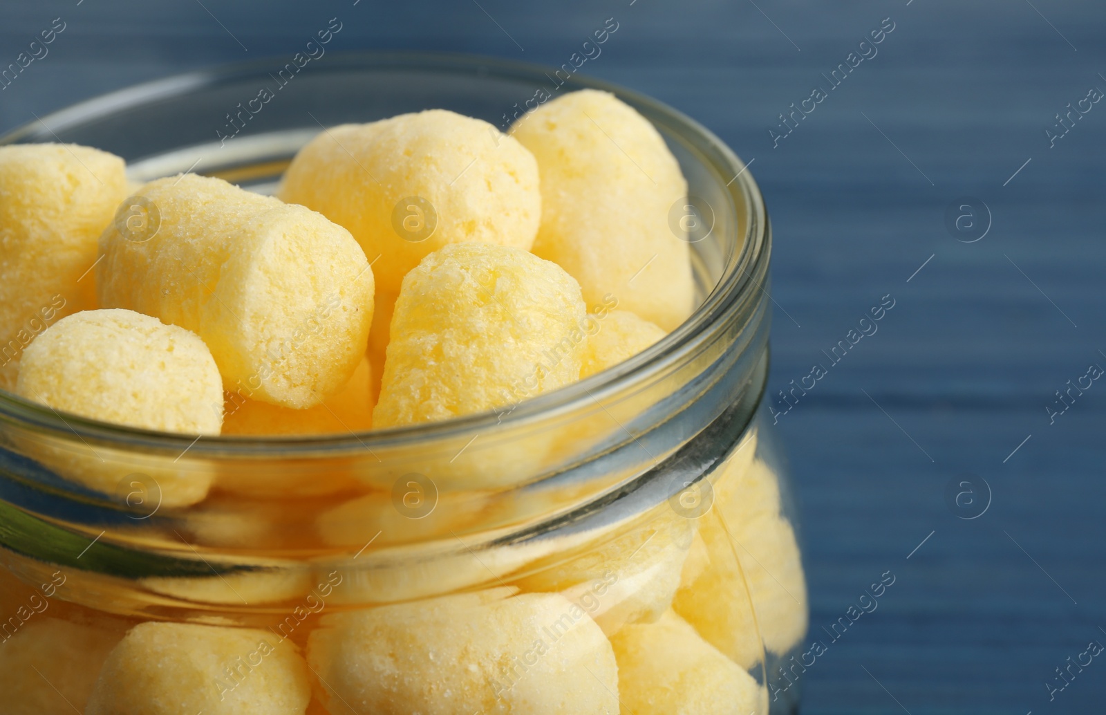 Photo of Jar of delicious crispy corn sticks on blue wooden table, closeup