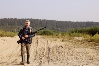 Photo of Man with hunting rifle outdoors. Space for text