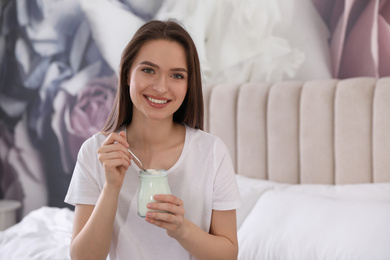 Photo of Young attractive woman with tasty yogurt on bed at home