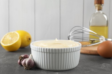 Photo of Fresh mayonnaise sauce in bowl and ingredients on grey table