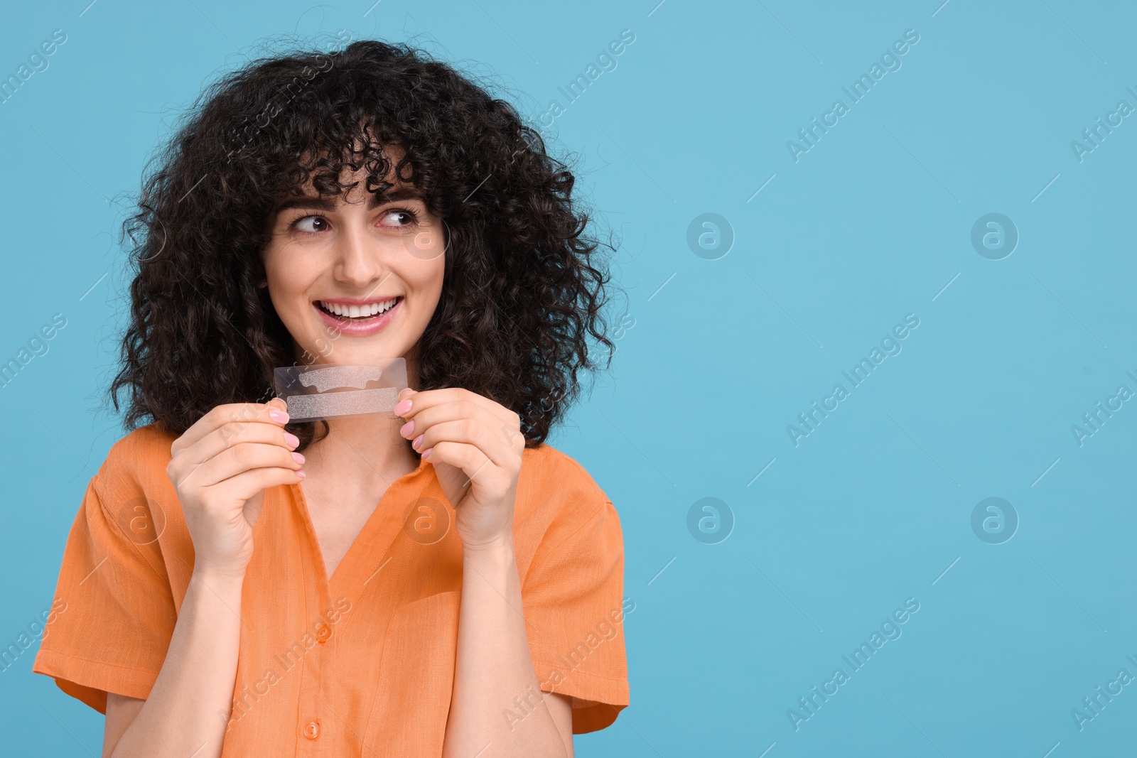 Photo of Young woman holding teeth whitening strips on light blue background, space for text