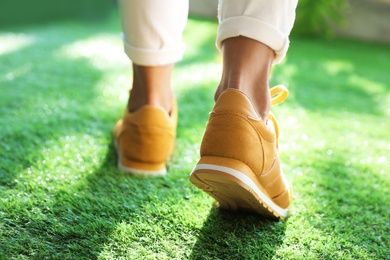 Young woman wearing stylish sneakers on green grass, closeup