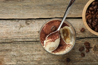 Photo of Delicious tiramisu in glass, spoon and coffee beans on wooden table, top view. Space for text