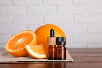 Bottles of essential oil with oranges on wooden table against white brick wall