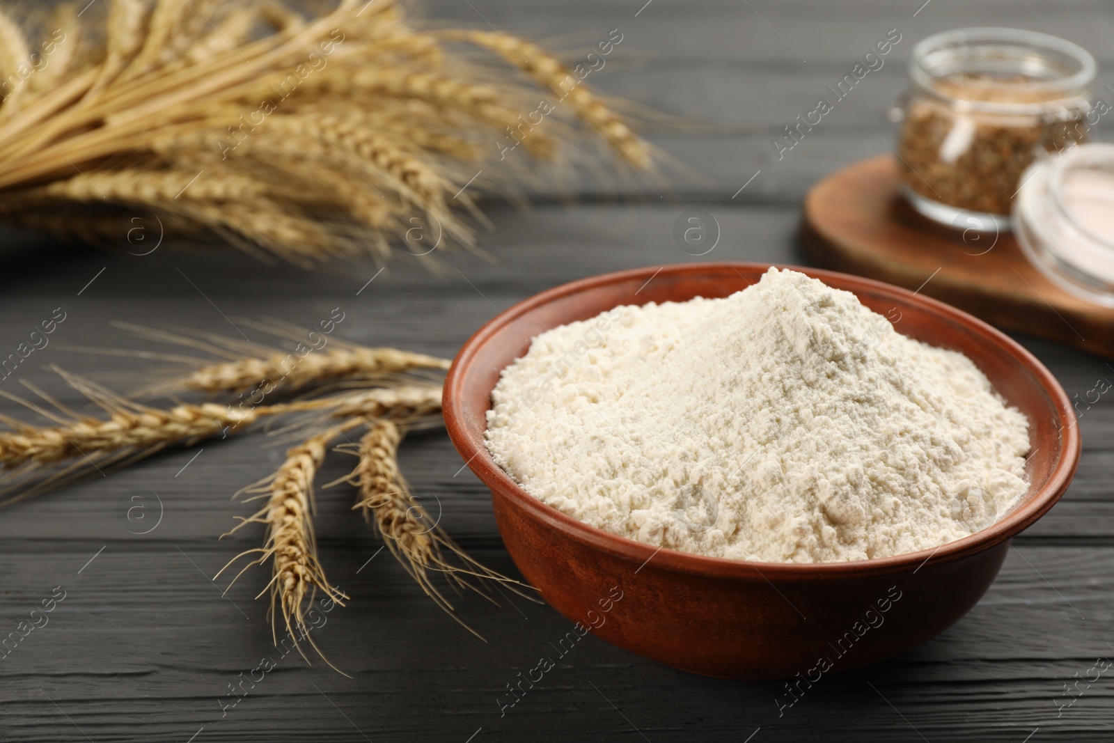 Photo of Bowl of flour and wheat ears on black wooden table. Space for text