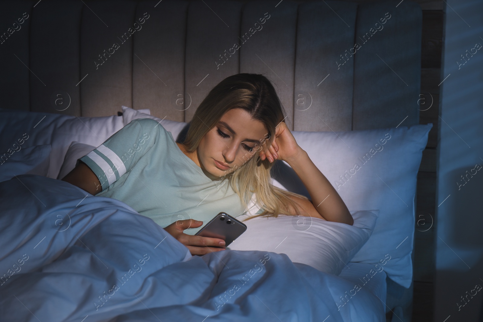 Photo of Young woman using smartphone in bed at night. Nomophobia and sleeping disorder problem