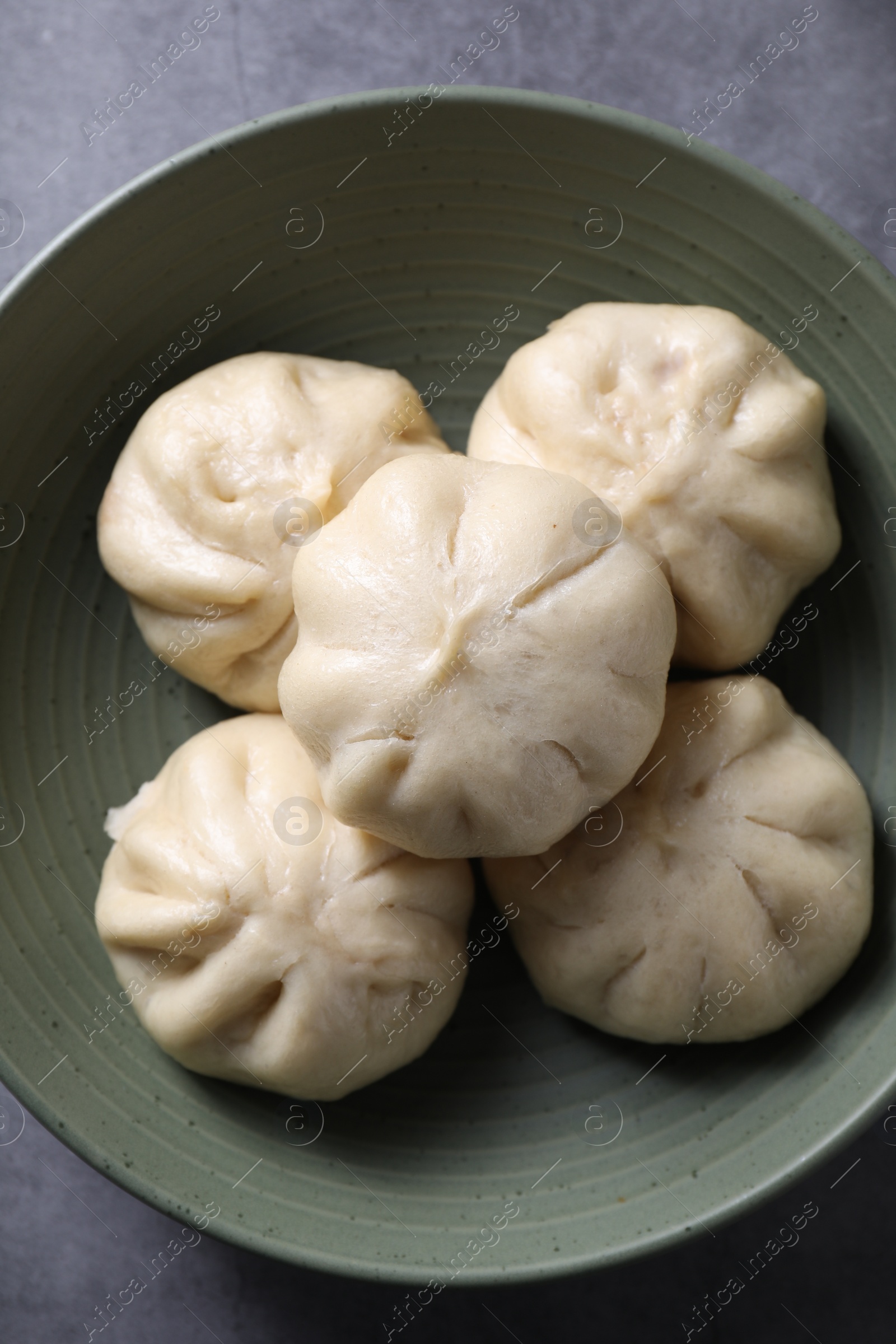 Photo of Delicious bao buns (baozi) in bowl on grey table, top view