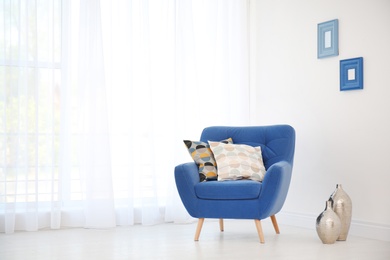 Photo of Armchair with different pillows near window in room