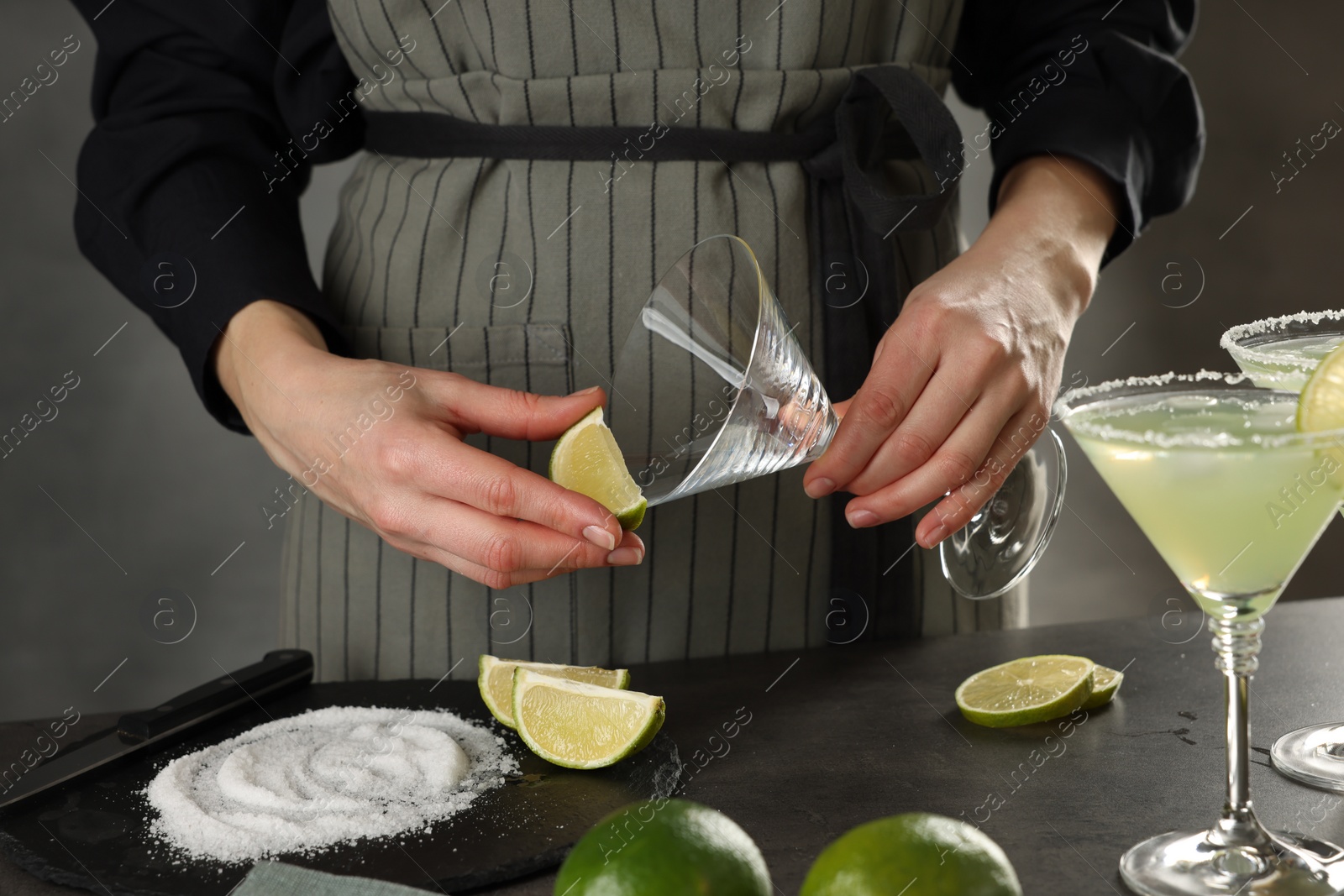 Photo of Woman making delicious Margarita cocktail at grey table, closeup