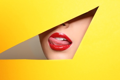 Photo of View of beautiful young woman with red lips through cutout in color paper, closeup