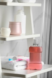 Photo of Bottle of mouthwash, toothpaste and brush on white shelf indoors