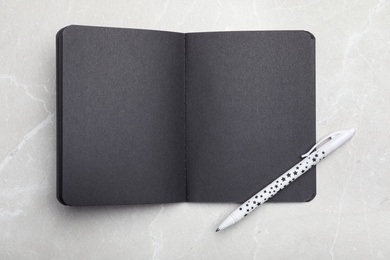 Photo of Stylish open black notebook and pen on marble table, top view