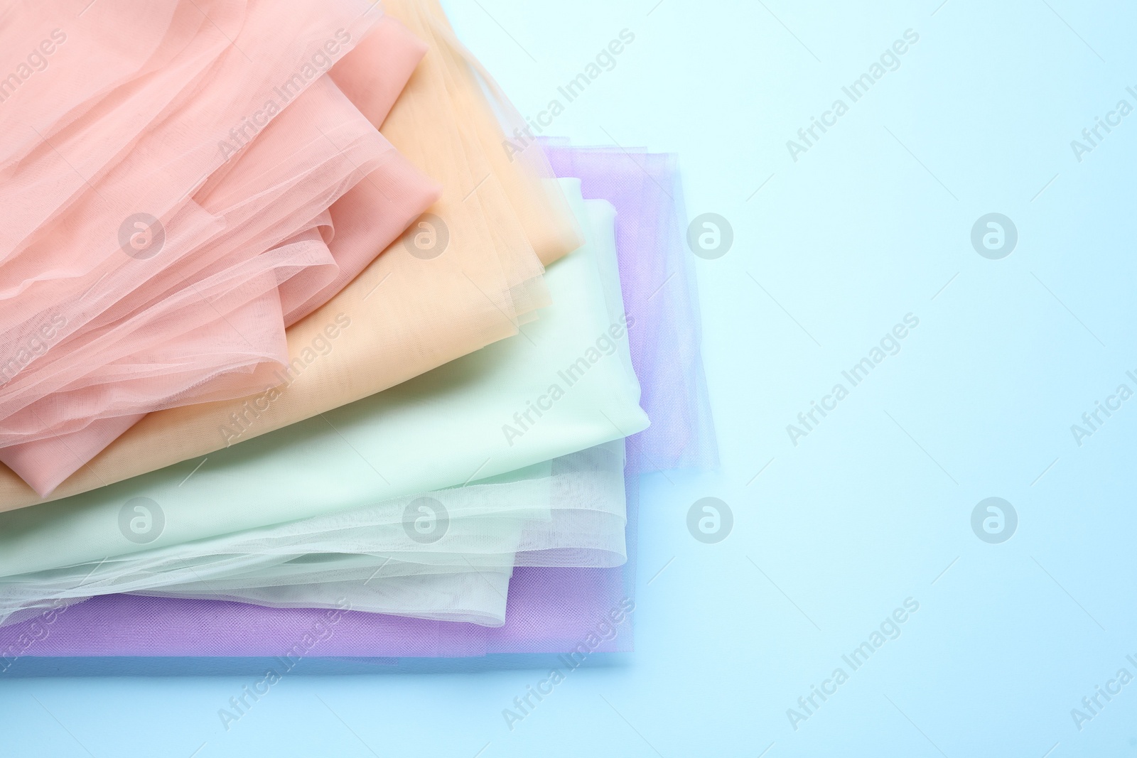 Photo of Beautiful colorful tulle fabrics on turquoise background. Space for text
