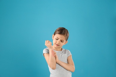 Photo of Little girl scratching forearm on color background. Allergy symptoms