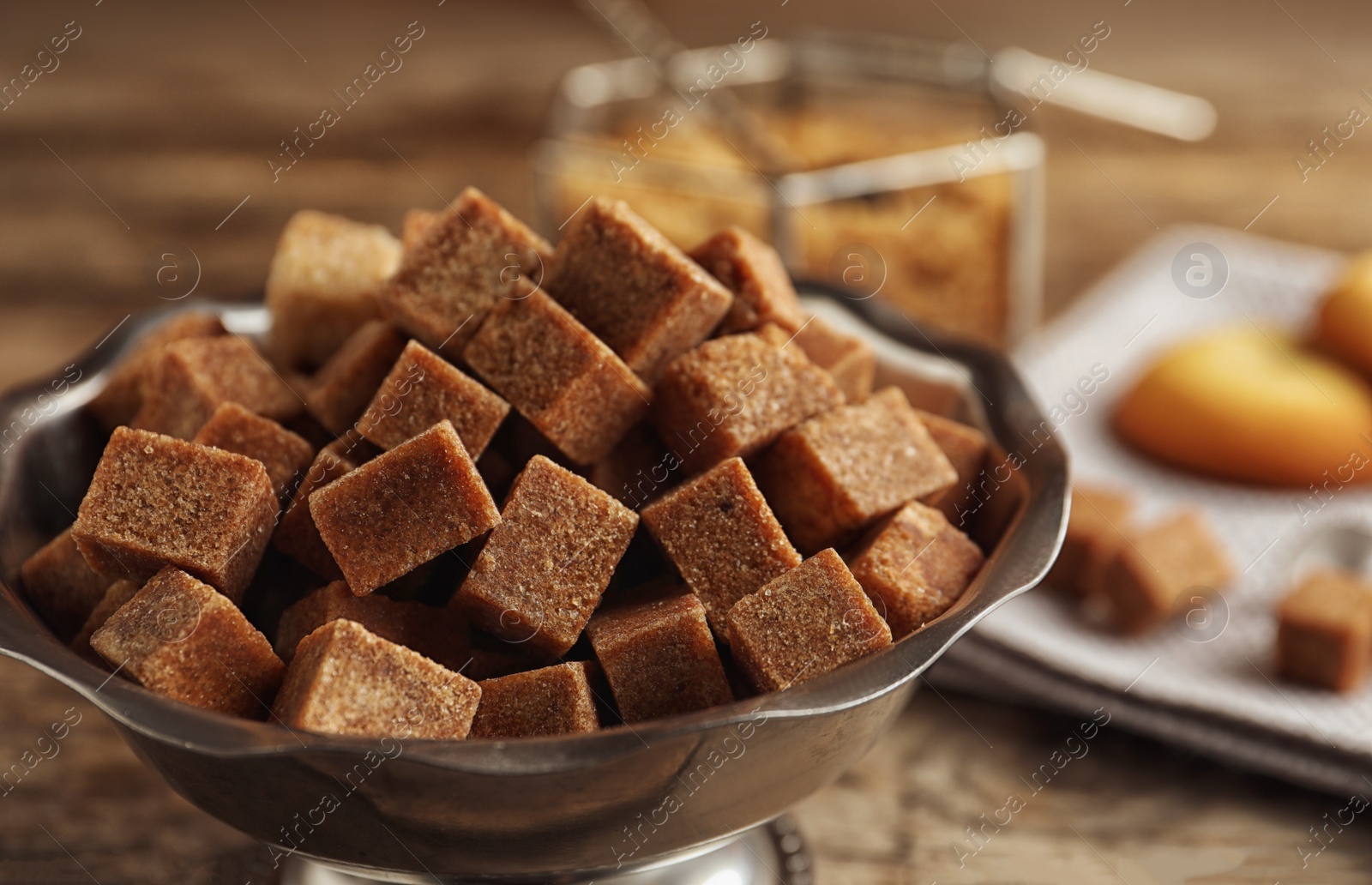 Photo of Brown sugar cubes in metal bowl on wooden table, closeup