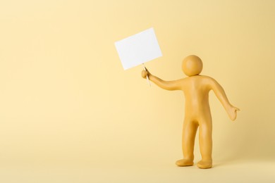 Photo of Human figure made of yellow plasticine holding blank sign on beige background. Space for text