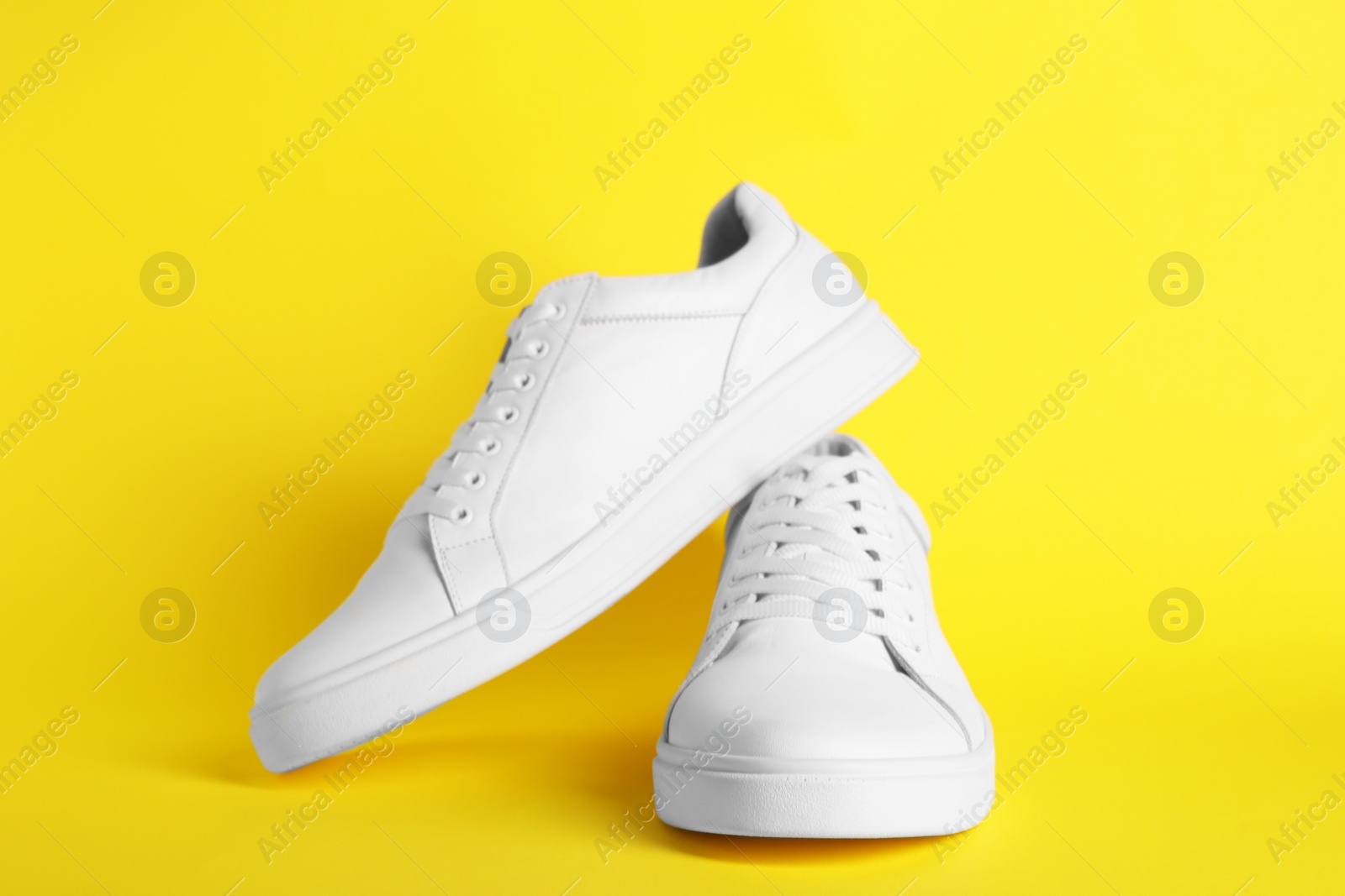 Photo of Pair of stylish white sneakers on yellow background